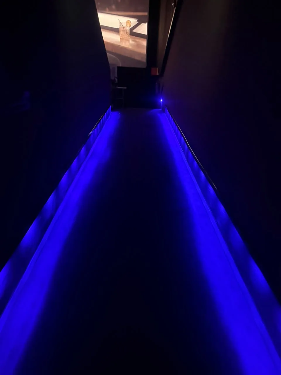Pasillo de acceso a sala de cine con guía LED azul en el piso