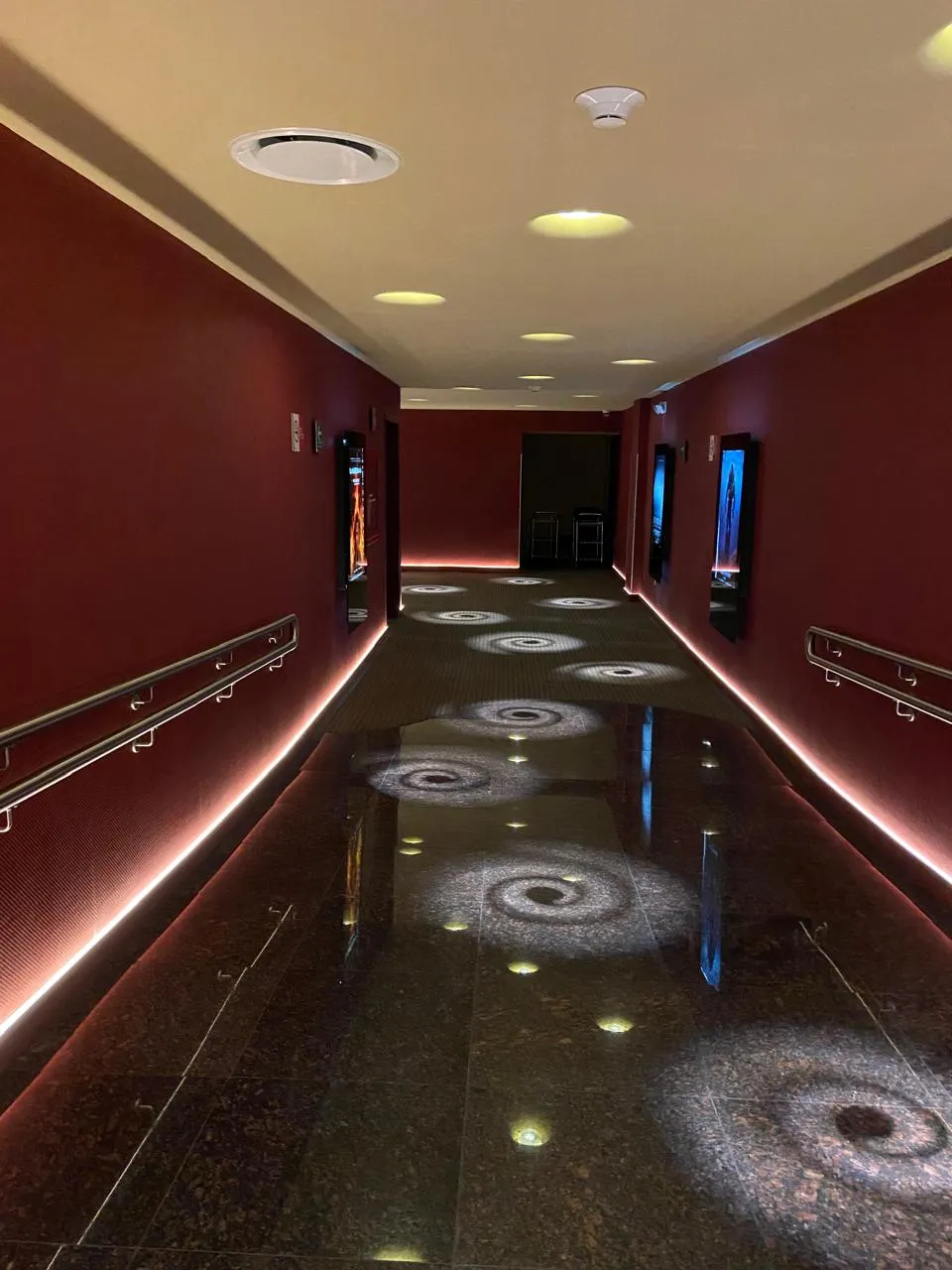 Pasillo de cine con cove light cálido y proyecciones circulares de luz en el piso