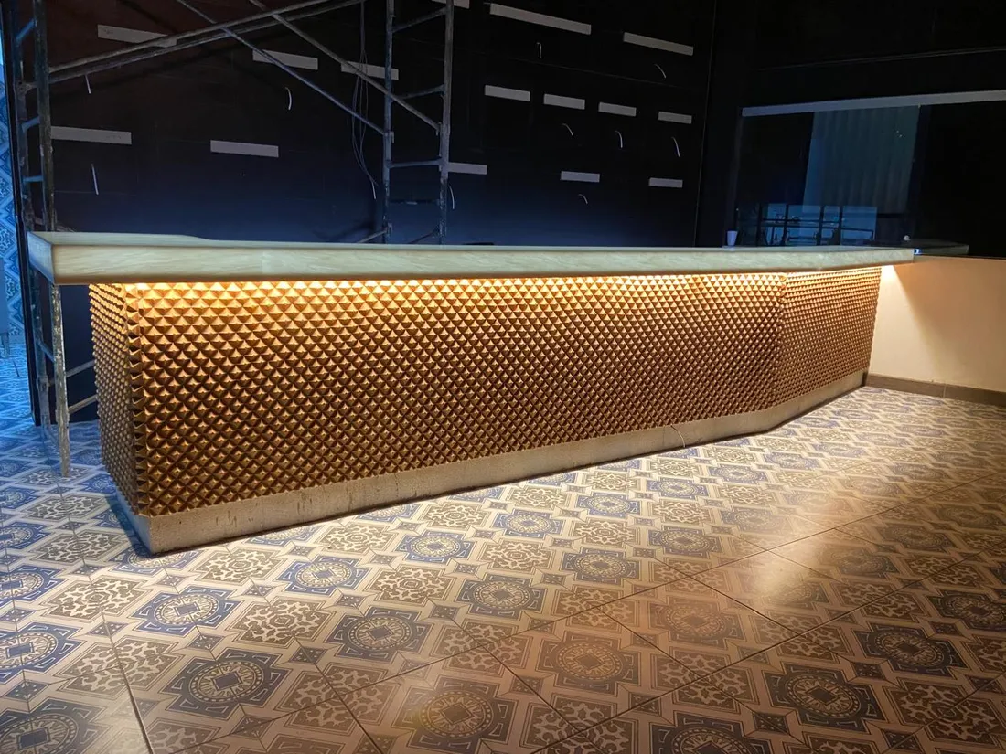 Barra con frente texturizado en tono dorado e iluminación indirecta cálida