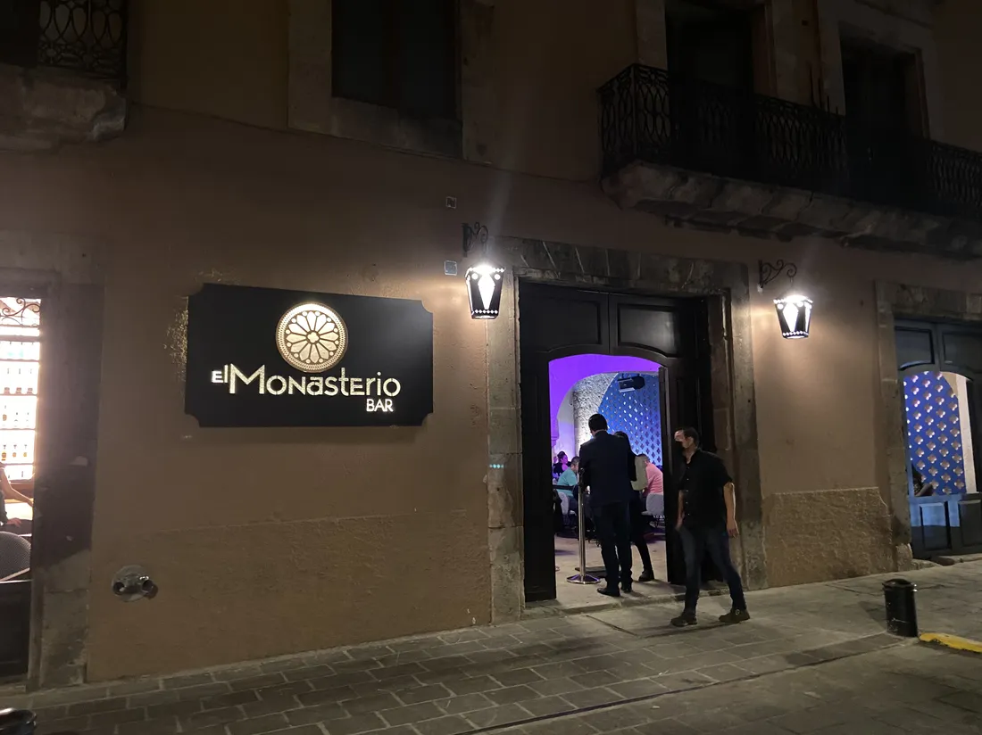 Fachada nocturna de bar con letrero iluminado y faroles laterales